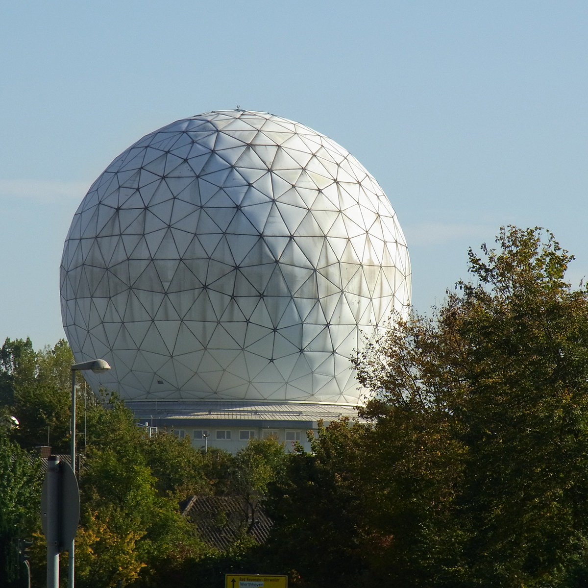 Große weiße Radarkuppel inmitten von Bäumen bei klarem Himmel.