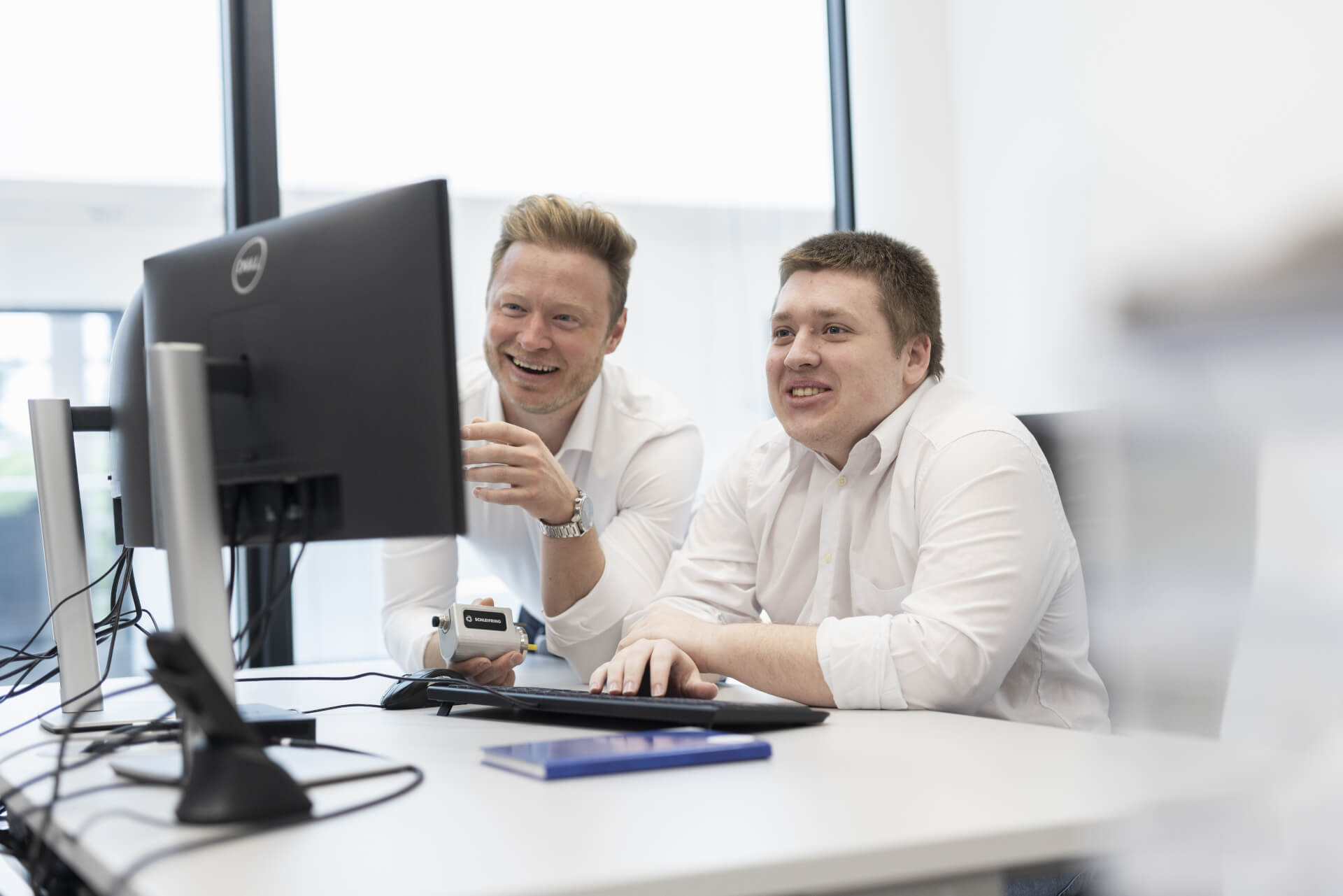 Ausbilder und Auszubildender arbeiten gemeinsam am Computer in moderner Büroumgebung.