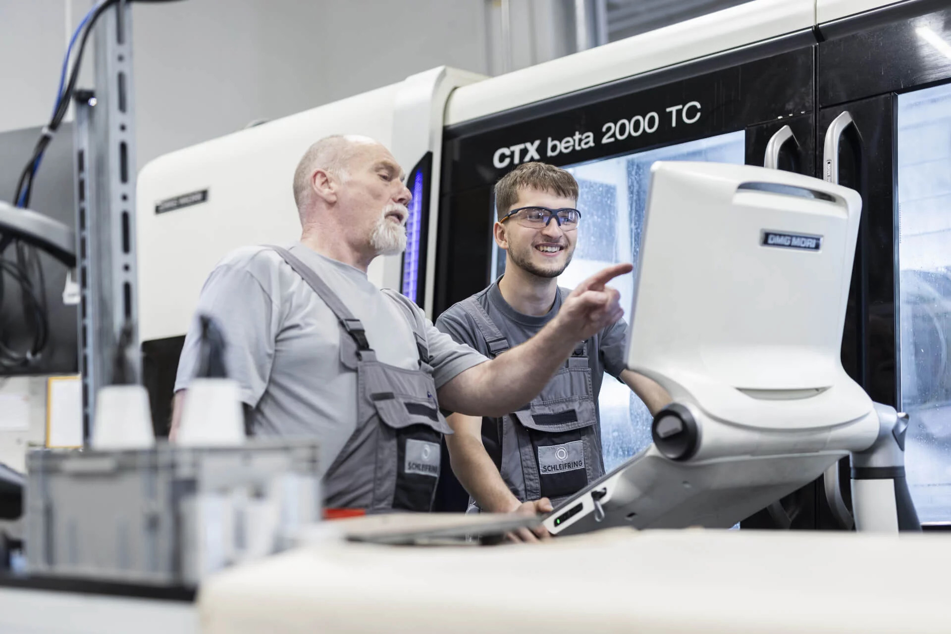 Ausbilder erklärt Auszubildendem die Steuerung einer CNC-Maschine vom Typ CTX beta 2000 TC.