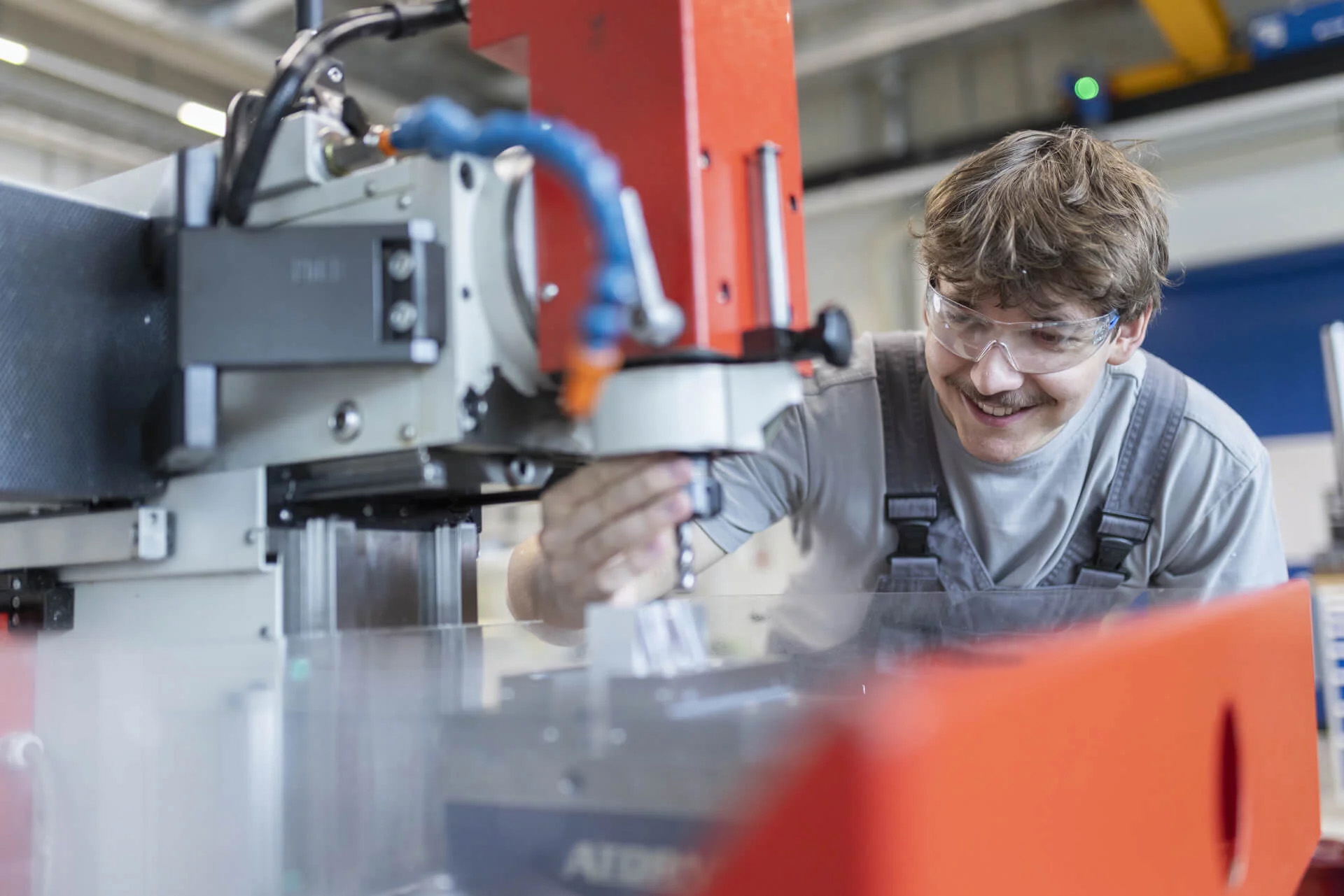 Auszubildender arbeitet konzentriert an einer CNC-Maschine und trägt eine Schutzbrille.