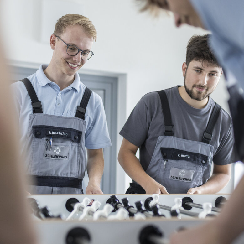 Auszubildende spielen gemeinsam Tischkicker in der Pause und haben sichtlich Spaß.