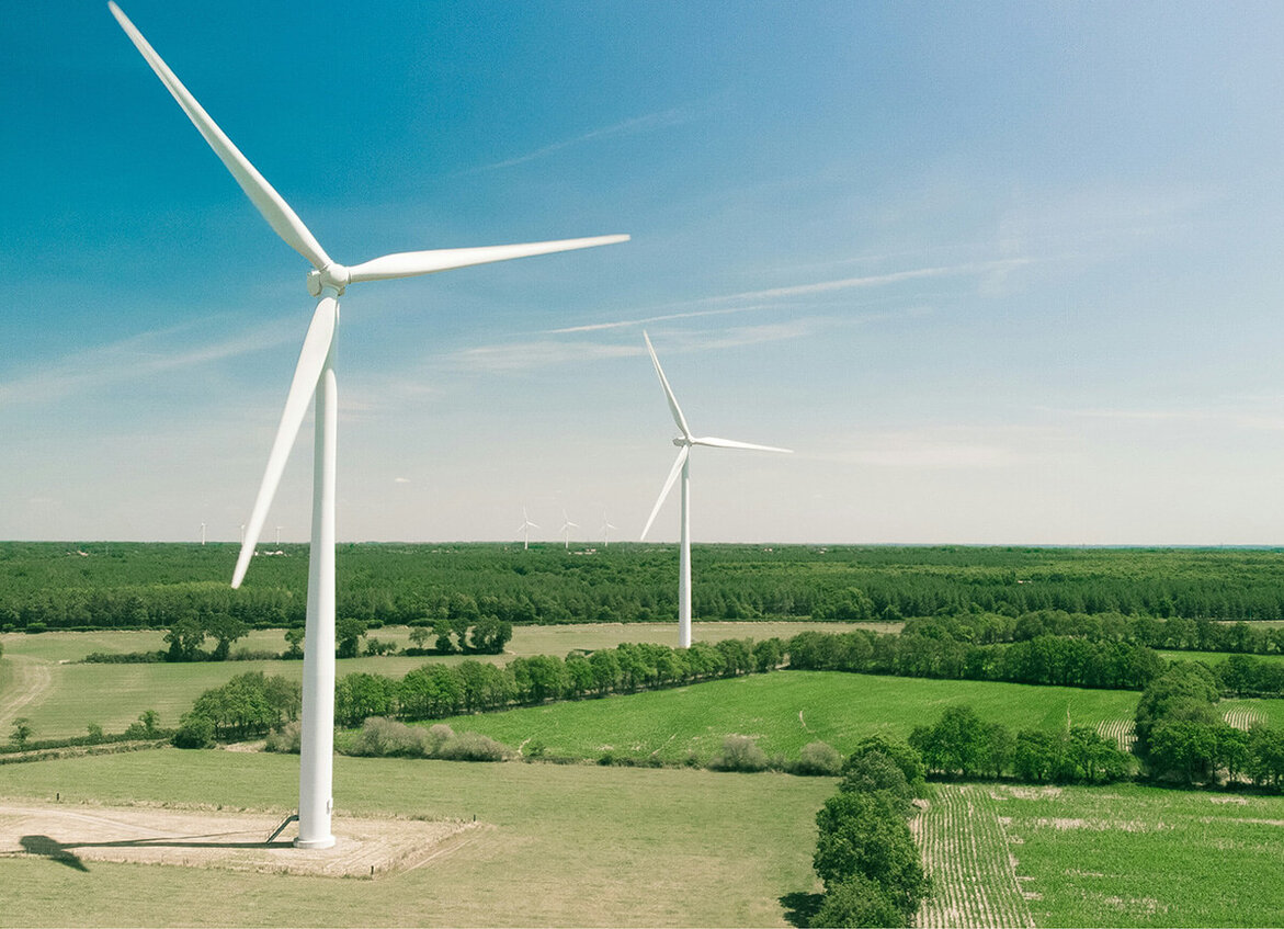 Zwei große Windräder stehen auf grünen Feldern unter blauem Himmel.