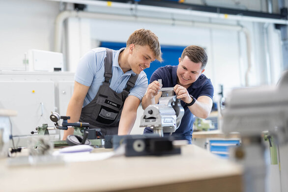 Zwei junge Männer arbeiten gemeinsam an einem Metallteil in einer Werkstatt.
