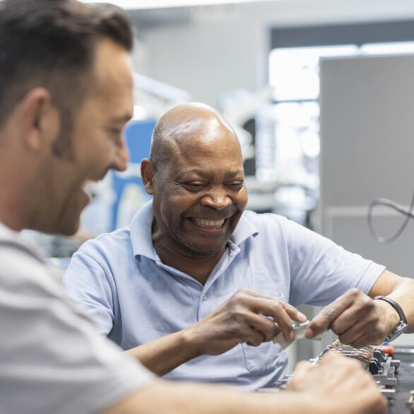 Zwei Mitarbeiter arbeiten gemeinsam und gut gelaunt an einem Elektronikbauteil in der Montage.